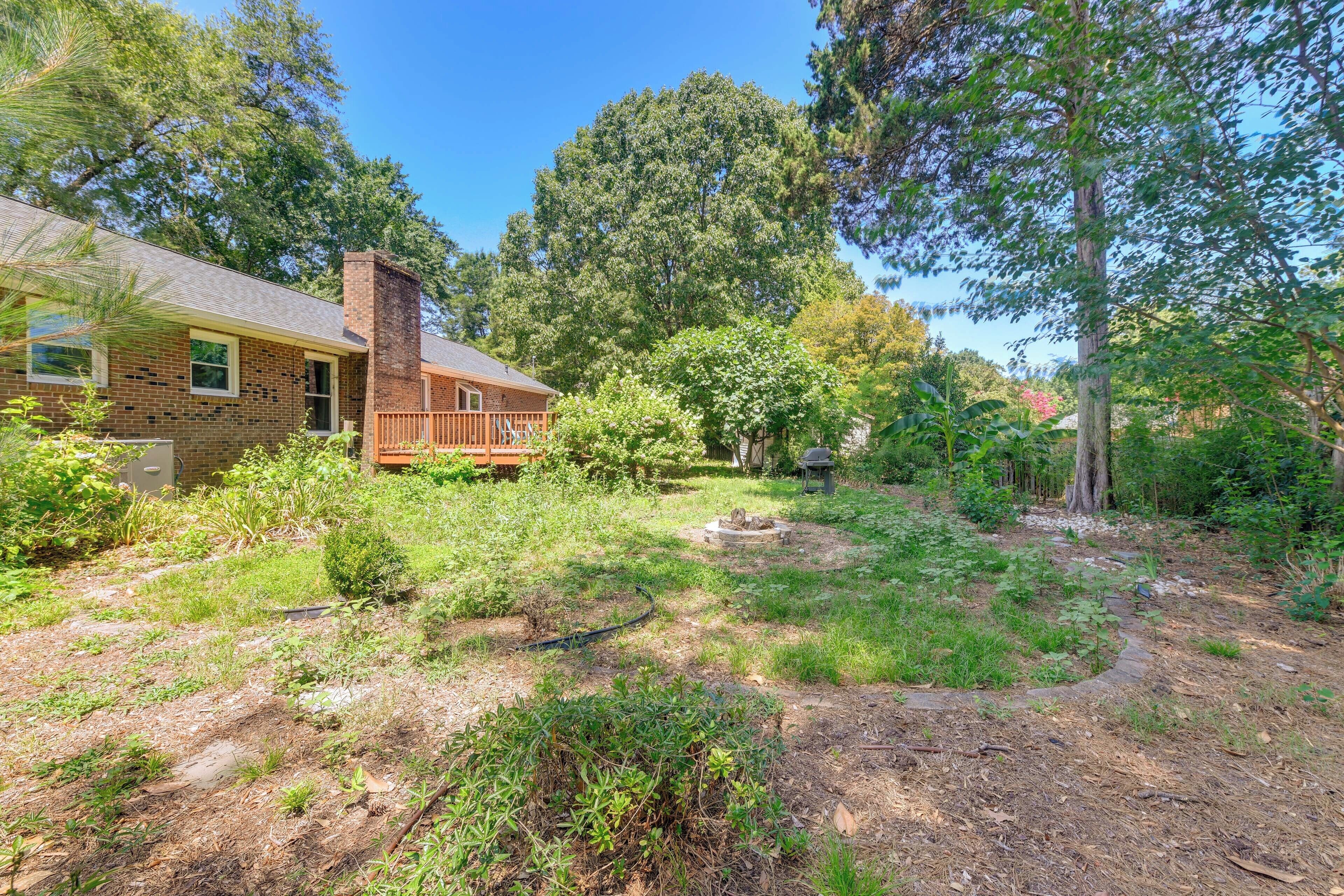 A house with a brick exterior, a wooden deck, and a garden area with trees and shrubs.