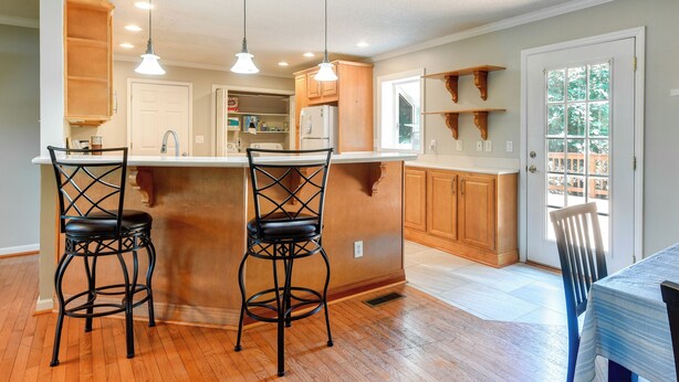 A kitchen with wooden cabinets, a white countertop, two black bar stools, and pendant lighting.