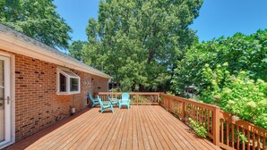 A wooden deck with a brick building, outdoor seating, and a wooden railing.