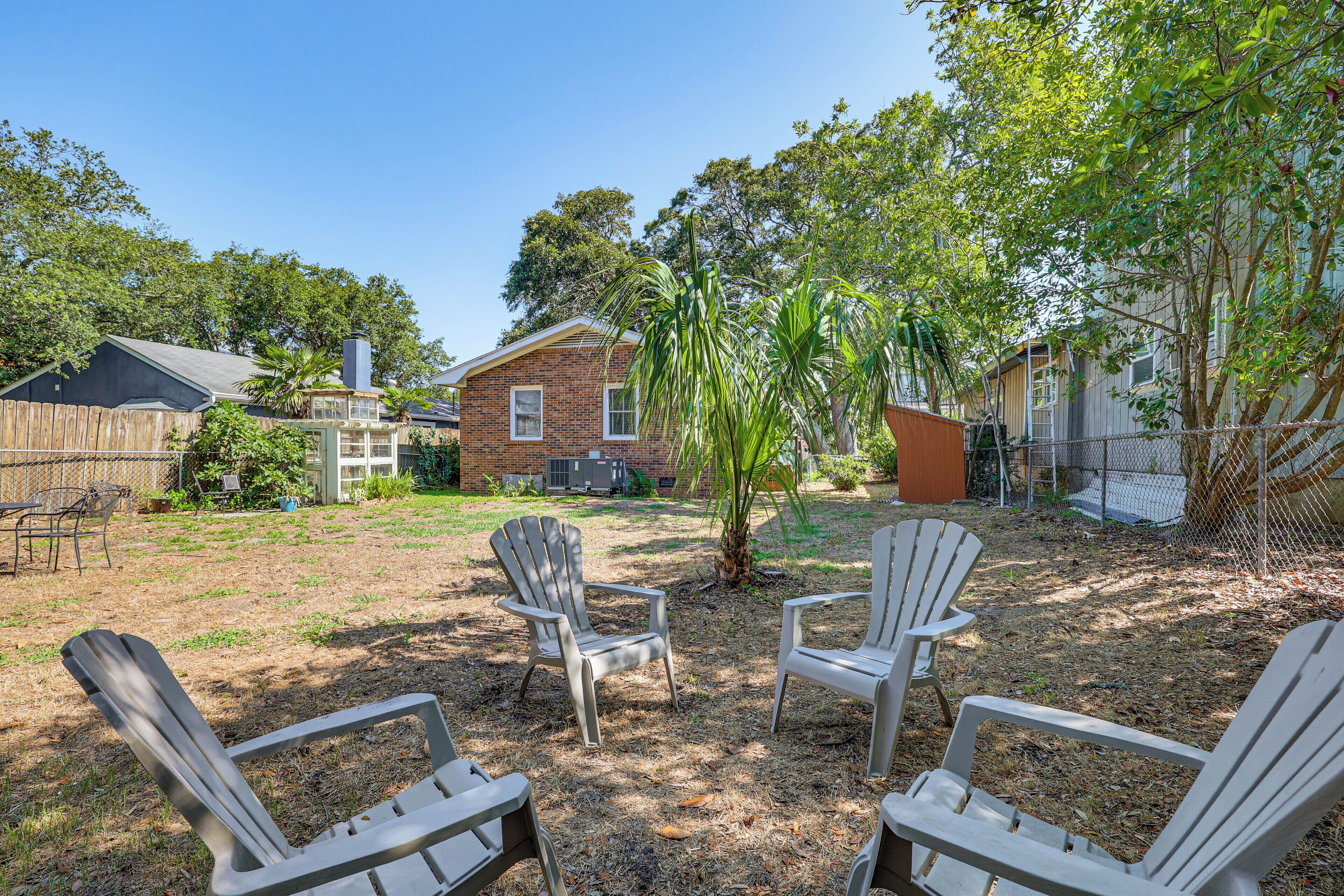 Un jardin avec quatre fauteuils Adirondack, une maison en briques et un espace clos avec des arbres.