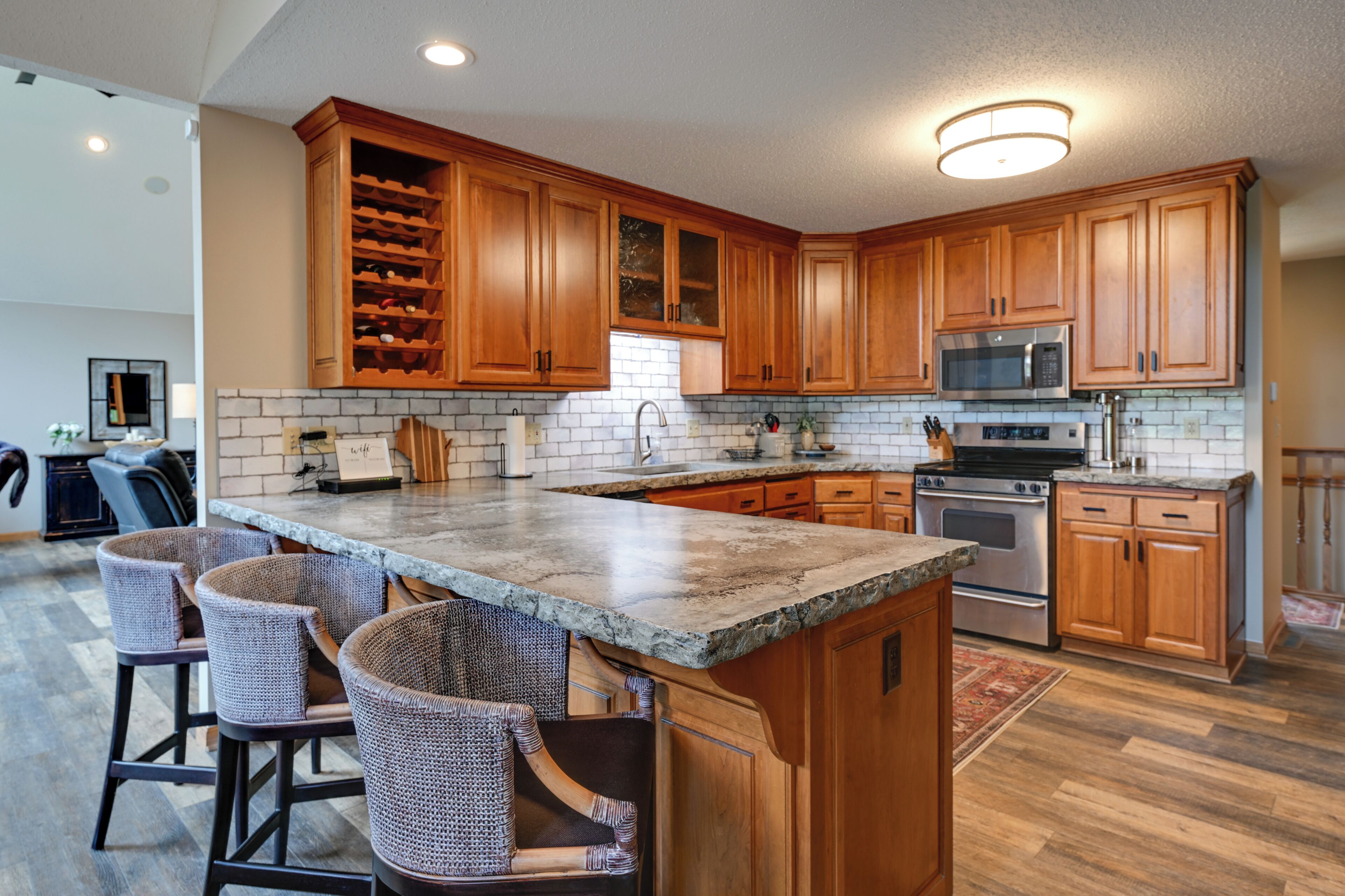 A kitchen with wooden cabinets, a granite countertop, a built-in wine rack, and a stainless steel oven.