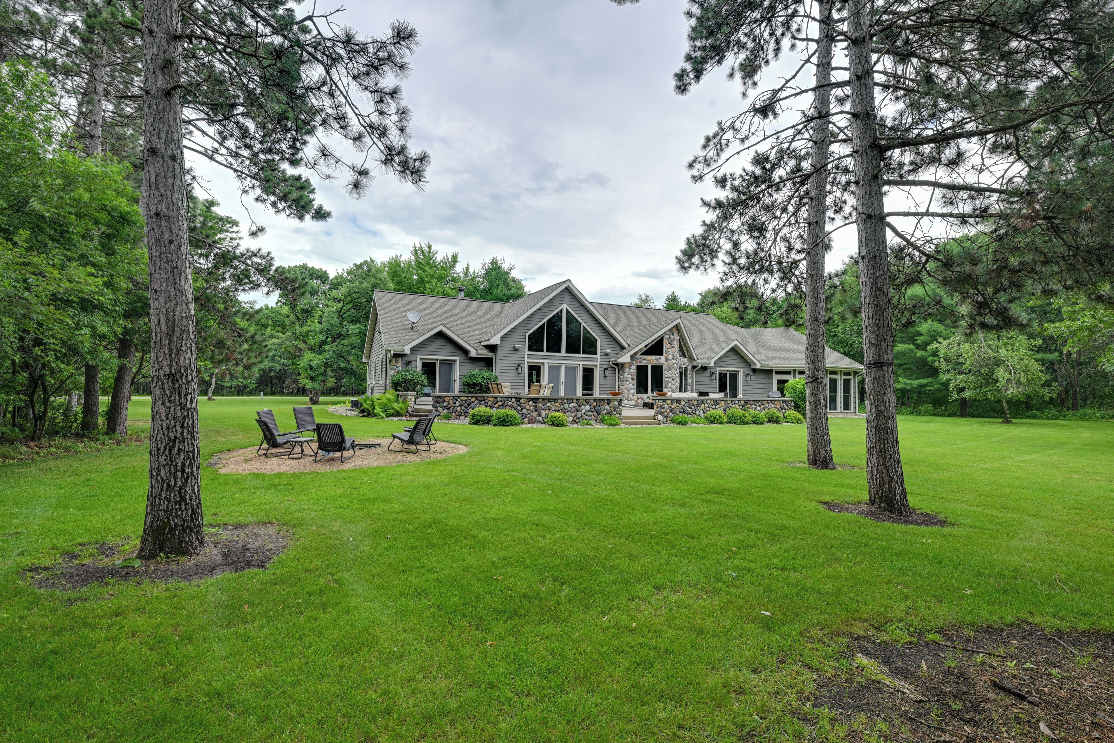 A large house with a stone foundation, a lawn, and a patio with chairs.