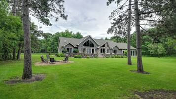 A large house with a stone foundation, a lawn, and a patio with chairs.