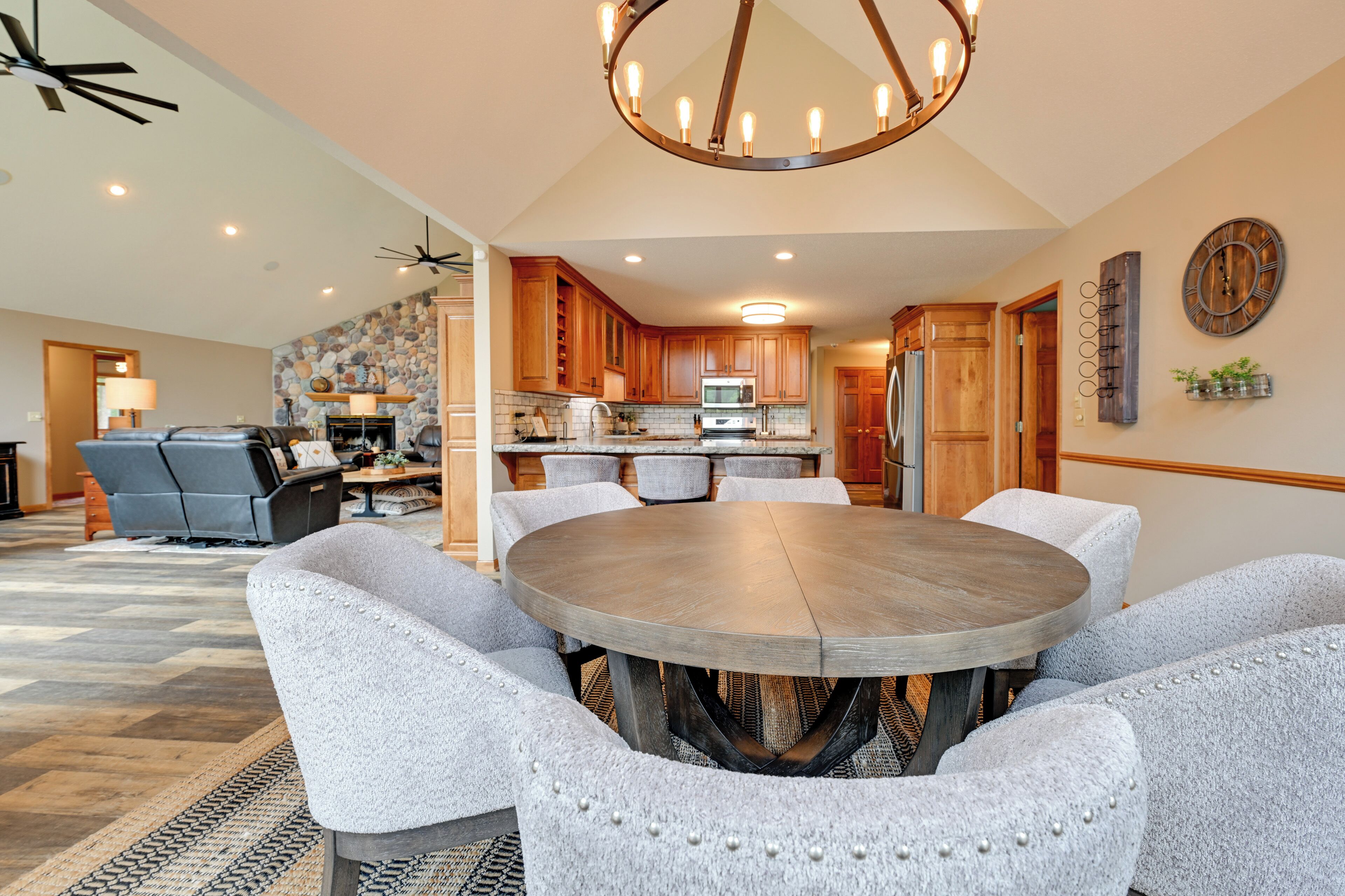 A dining area with a round table and upholstered chairs, a kitchen with wooden cabinets, and a stone accent wall.