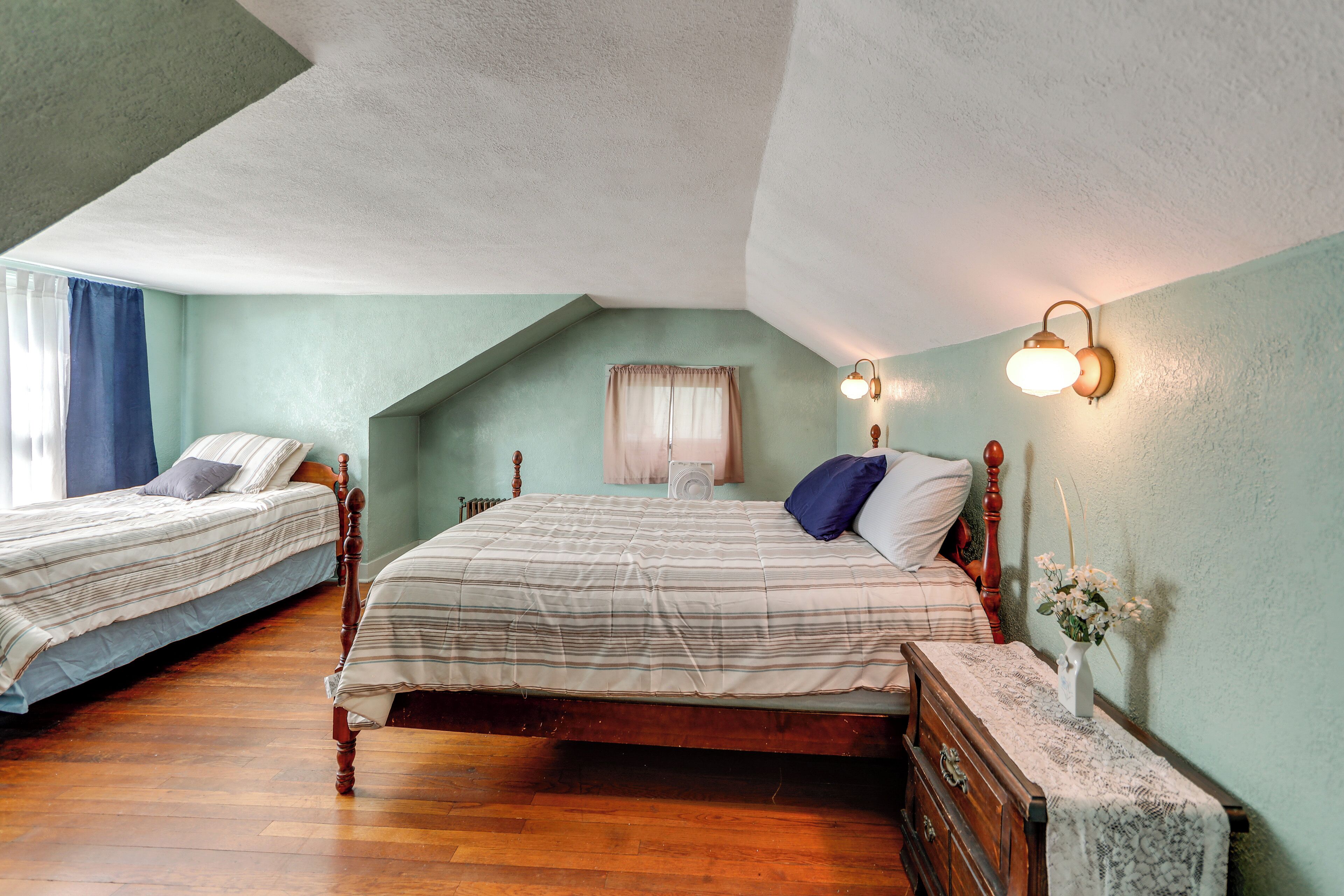 Een slaapkamer met twee bedden, een houten dressoir, een nachtkastje met een vaas en een plafondventilator.