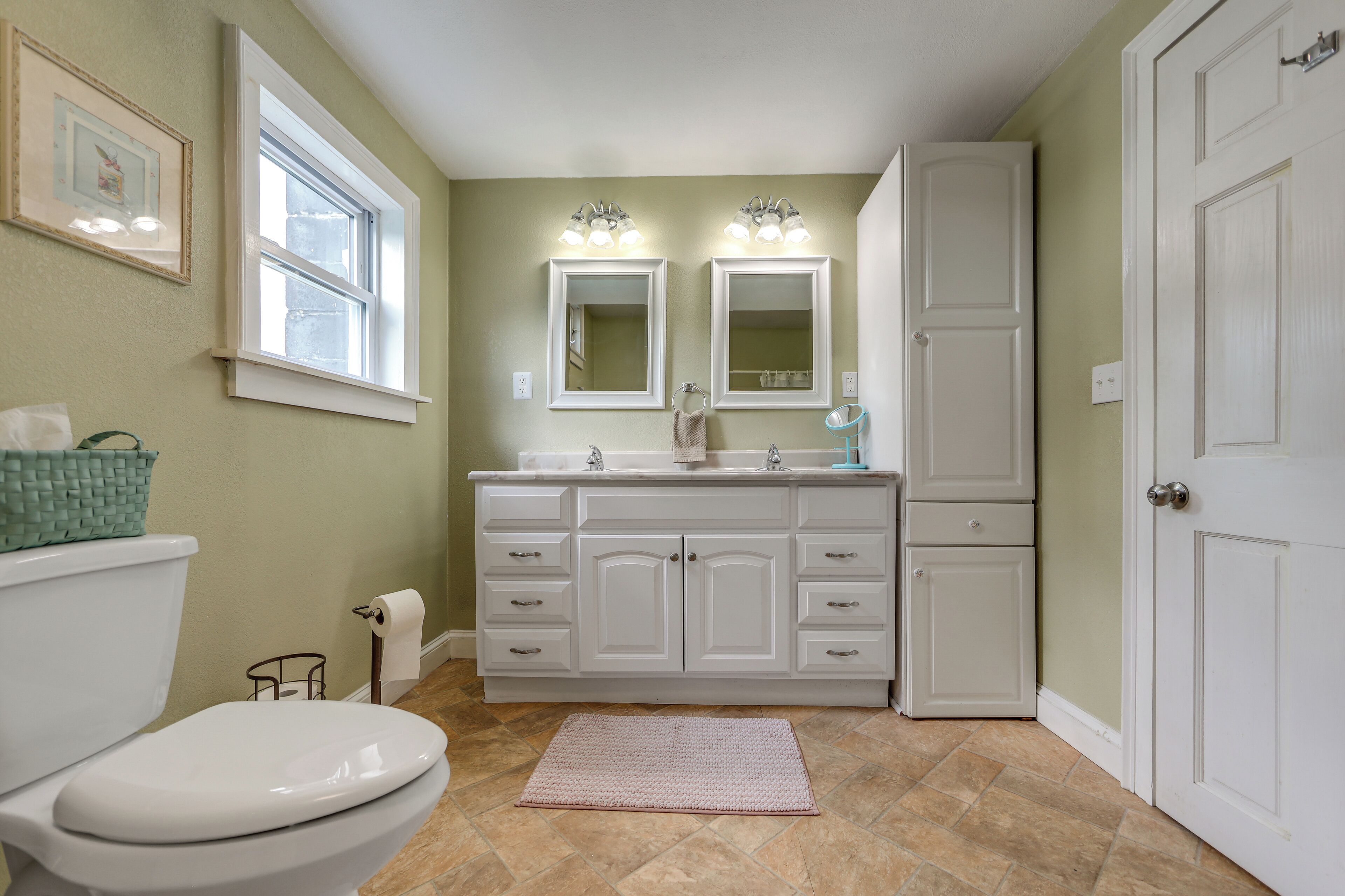 A bathroom with a toilet, vanity, double sink, and a door.