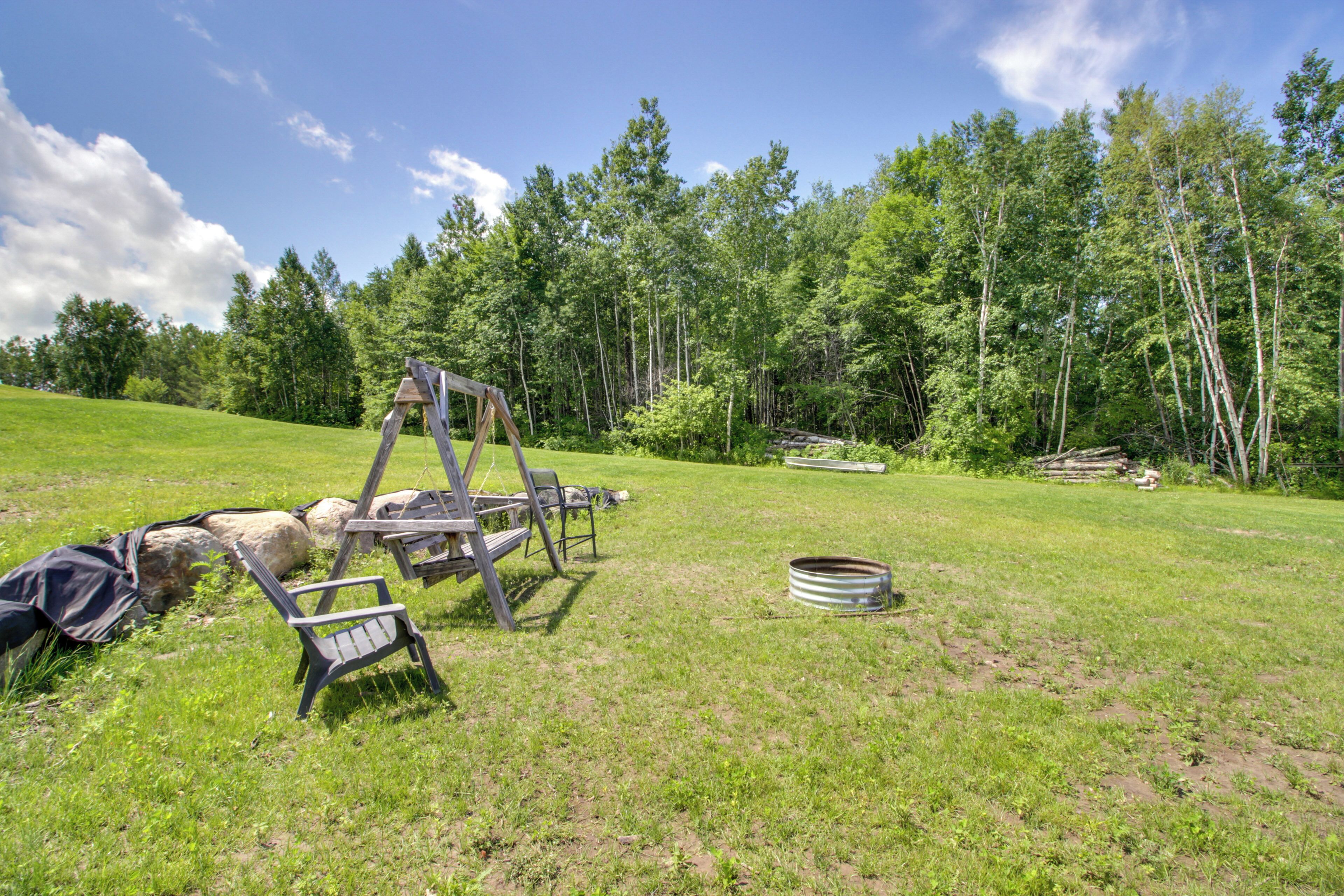 A grassy outdoor area with a swing set, a metal barrel, and a wooden structure.