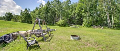 A grassy outdoor area with a swing set, a metal barrel, and a wooden structure.