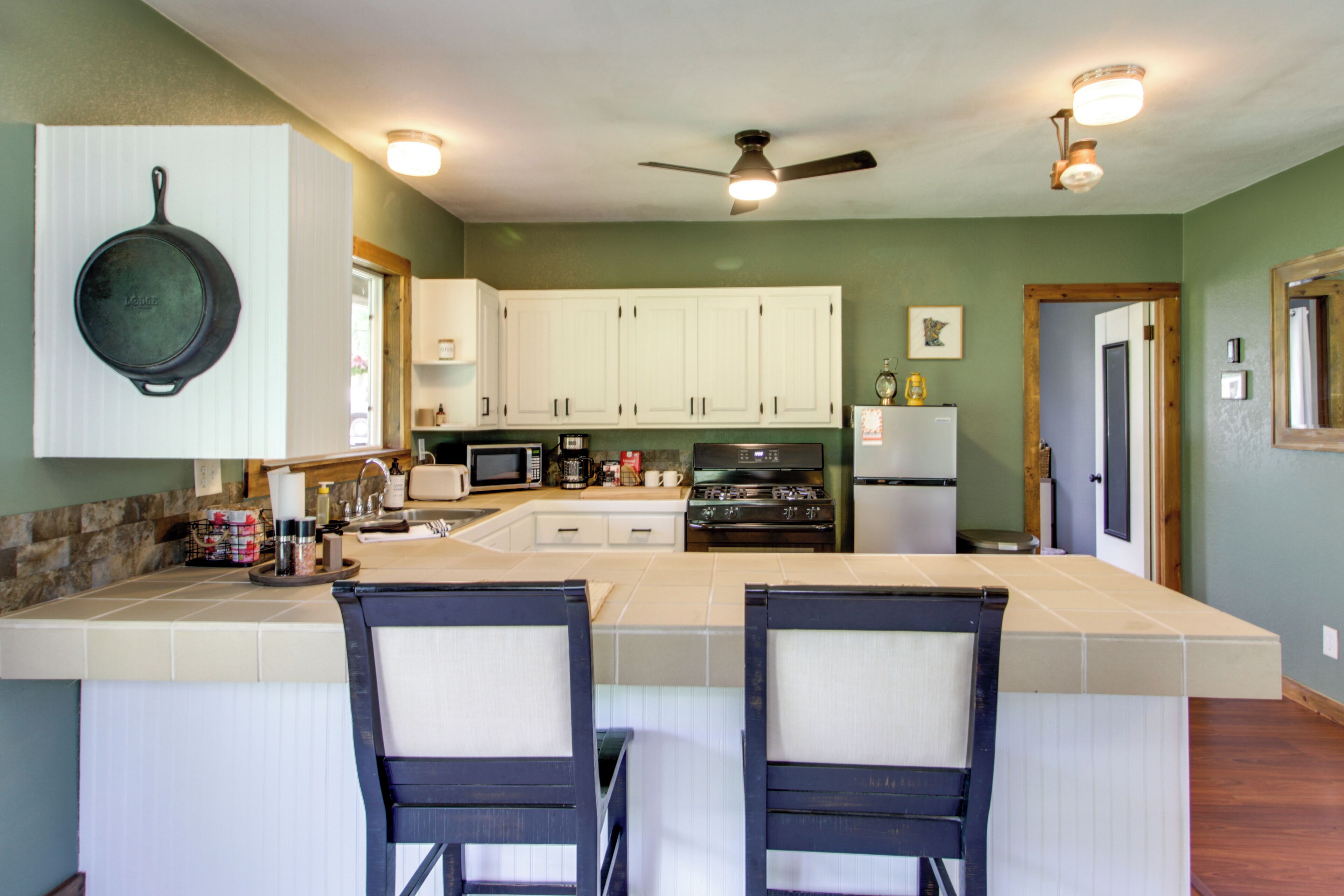 A kitchen with white cabinets, a microwave, a stove, and a refrigerator. There is a ceiling fan and recessed lighting.