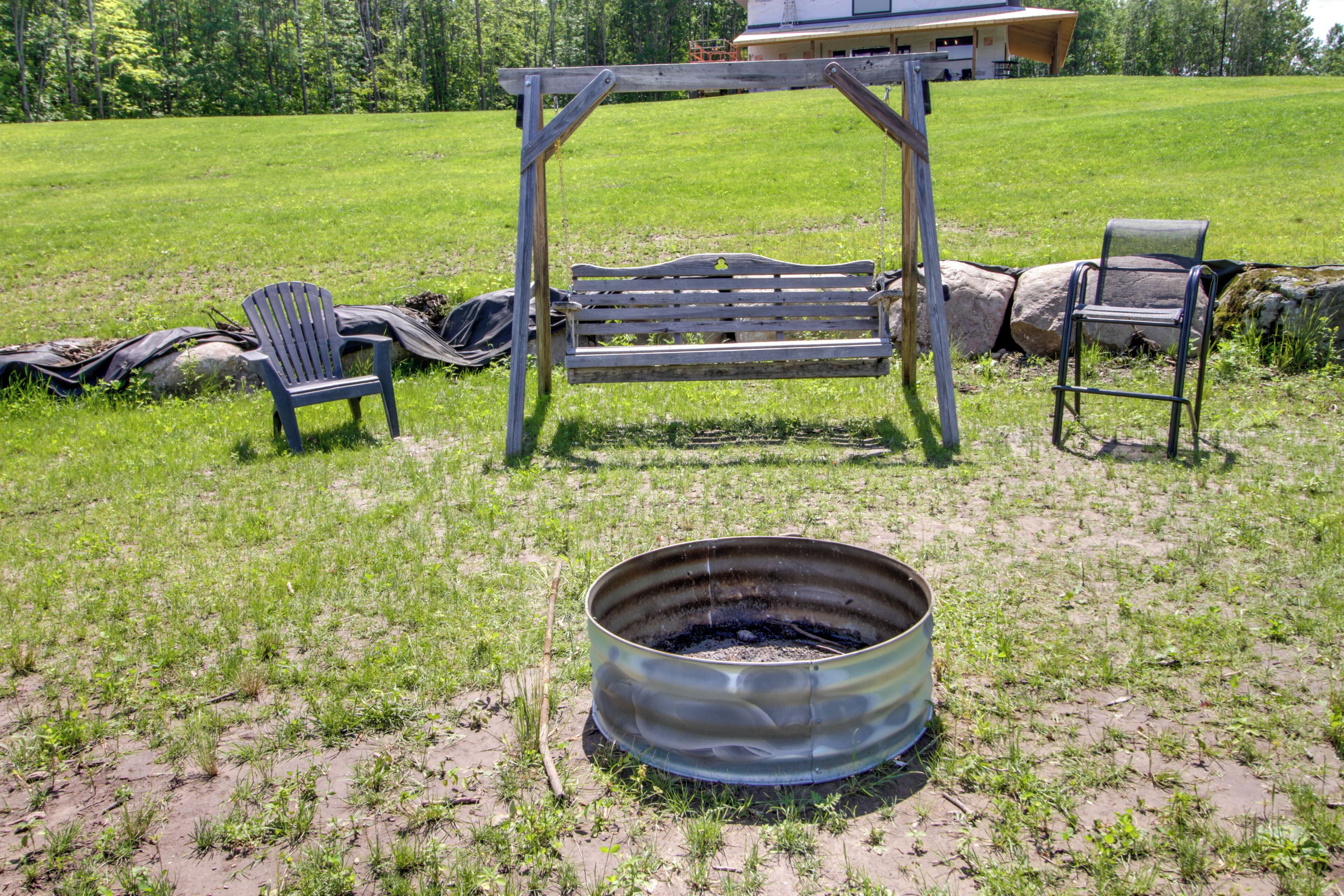 A rustic outdoor setting with a swing, two Adirondack chairs, and a metal fire pit.