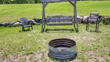 A rustic outdoor setting with a swing, two Adirondack chairs, and a metal fire pit.