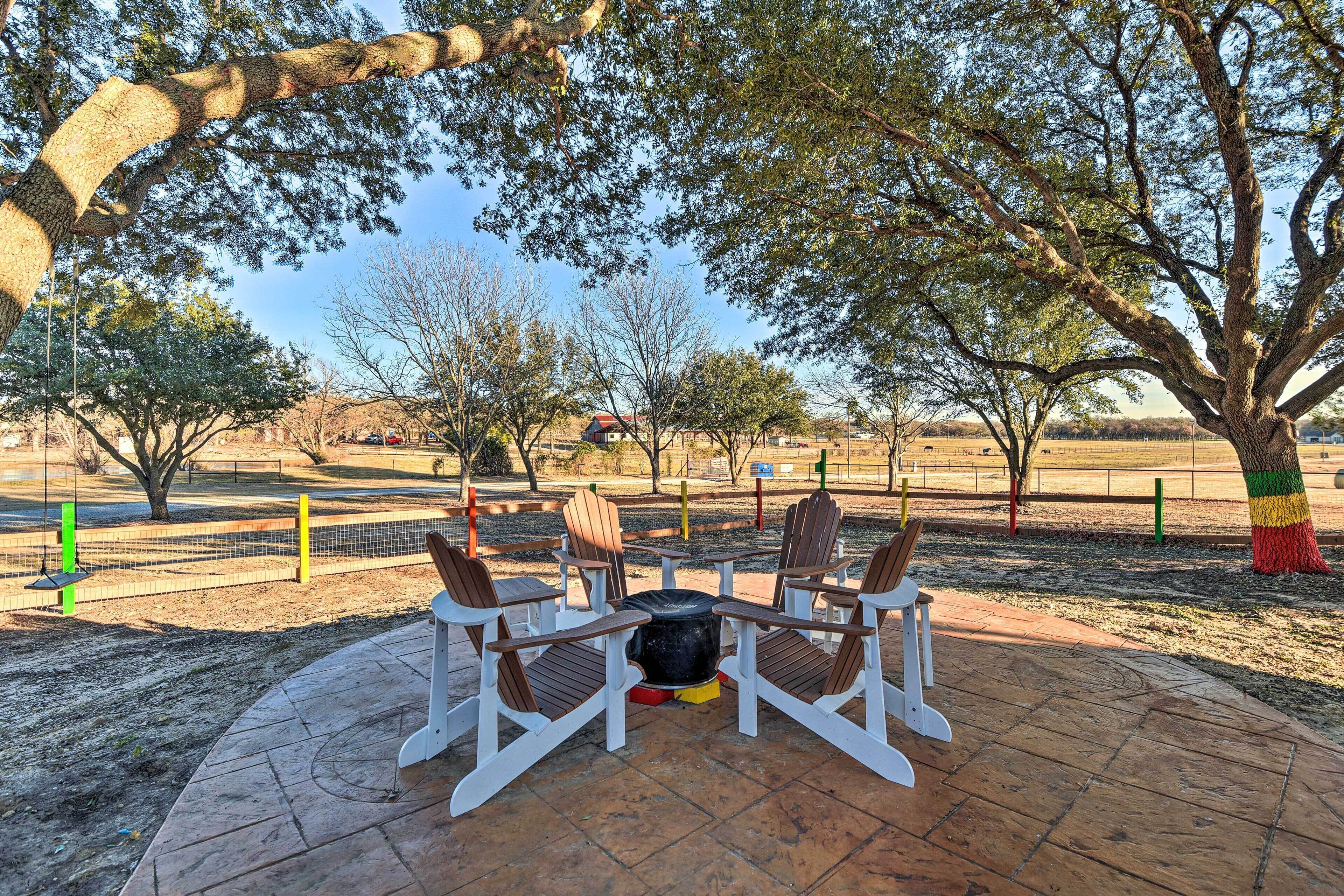 Un patio con un hogar para fogata y cuatro sillas Adirondack.