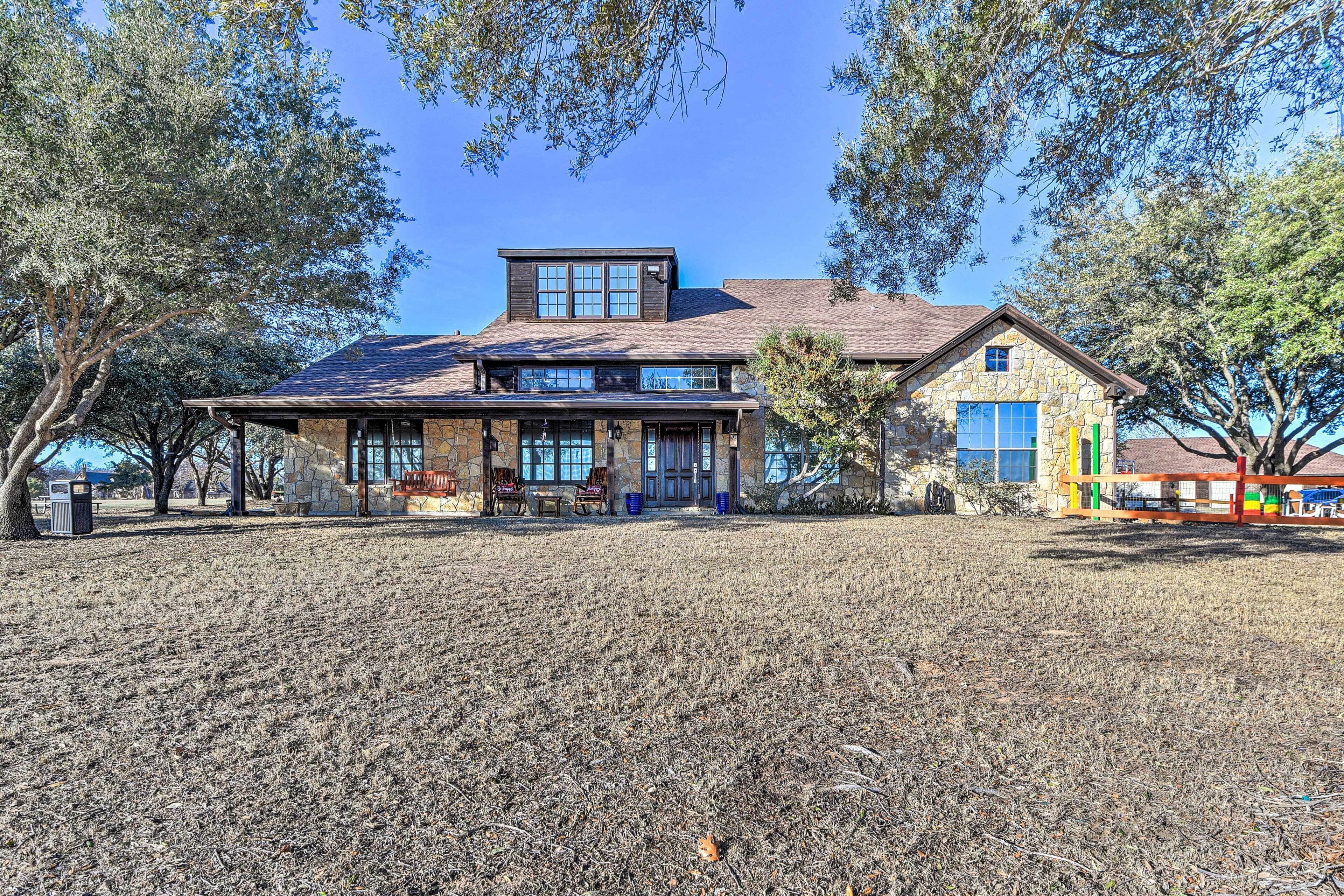 A two-story house with a stone facade, large windows, and a covered patio area.