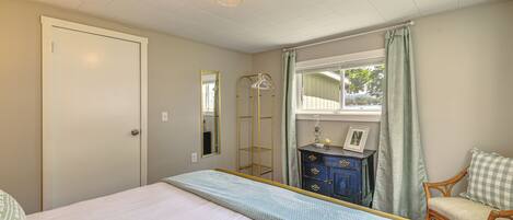 A bedroom with a bed, a dresser, a mirror, a window with curtains, and a door.