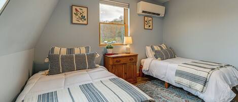 A bedroom with two beds, a window, an air conditioner, and a rug.