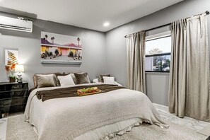 Ein Schlafzimmer mit einem Bett, einem Nachttisch, einer Lampe, einem Gemälde und einem Fenster mit Vorhängen.