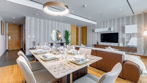 Un espace repas moderne avec une table en marbre, des chaises blanches et un grand téléviseur à écran plat fixé au mur.