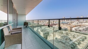 Un balcon doté d'une balustrade en verre, de meubles en osier et offrant une vue sur le paysage urbain.