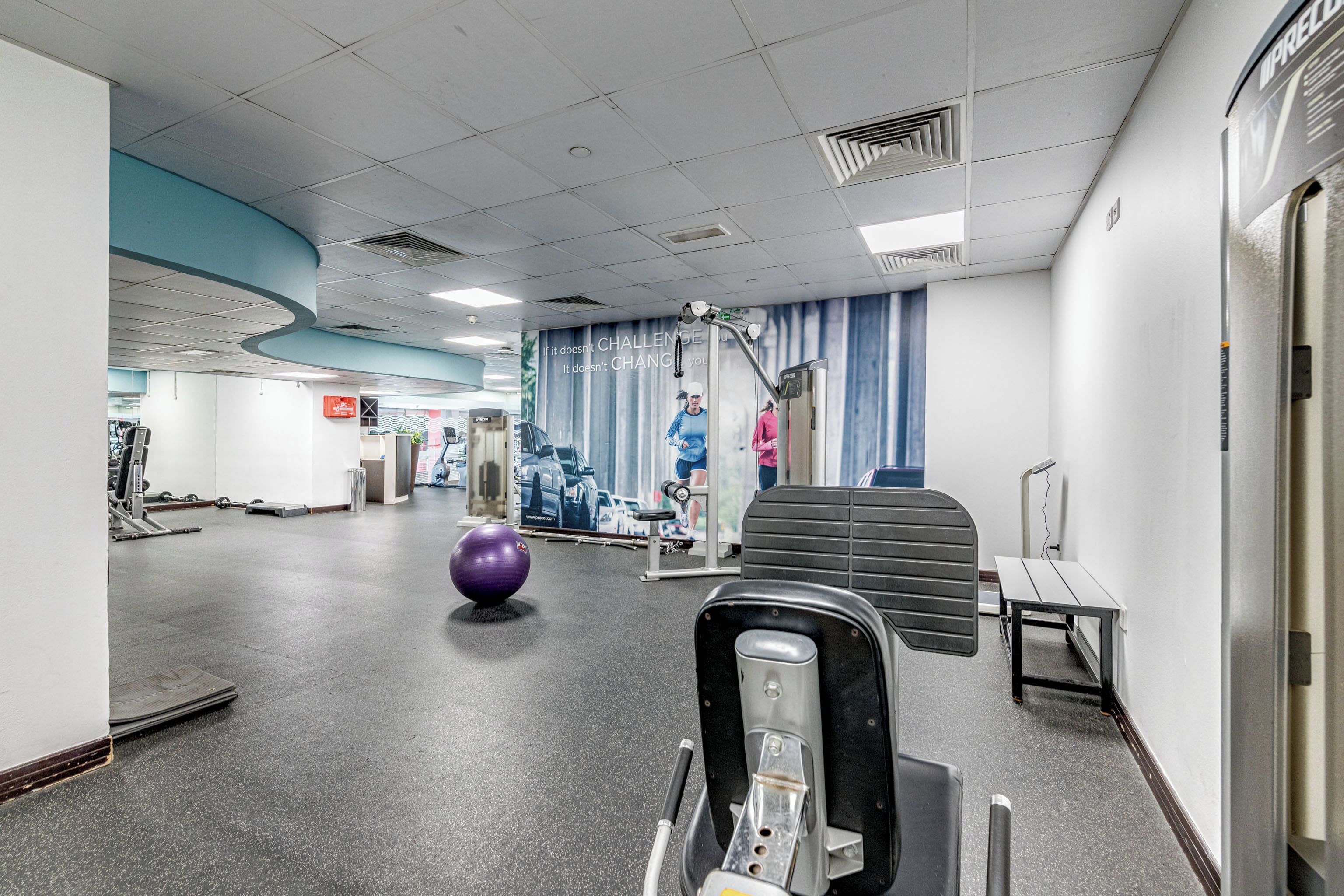 Een fitnessruimte met trainingsapparatuur, een groot poster en een paarse fitnessbal.