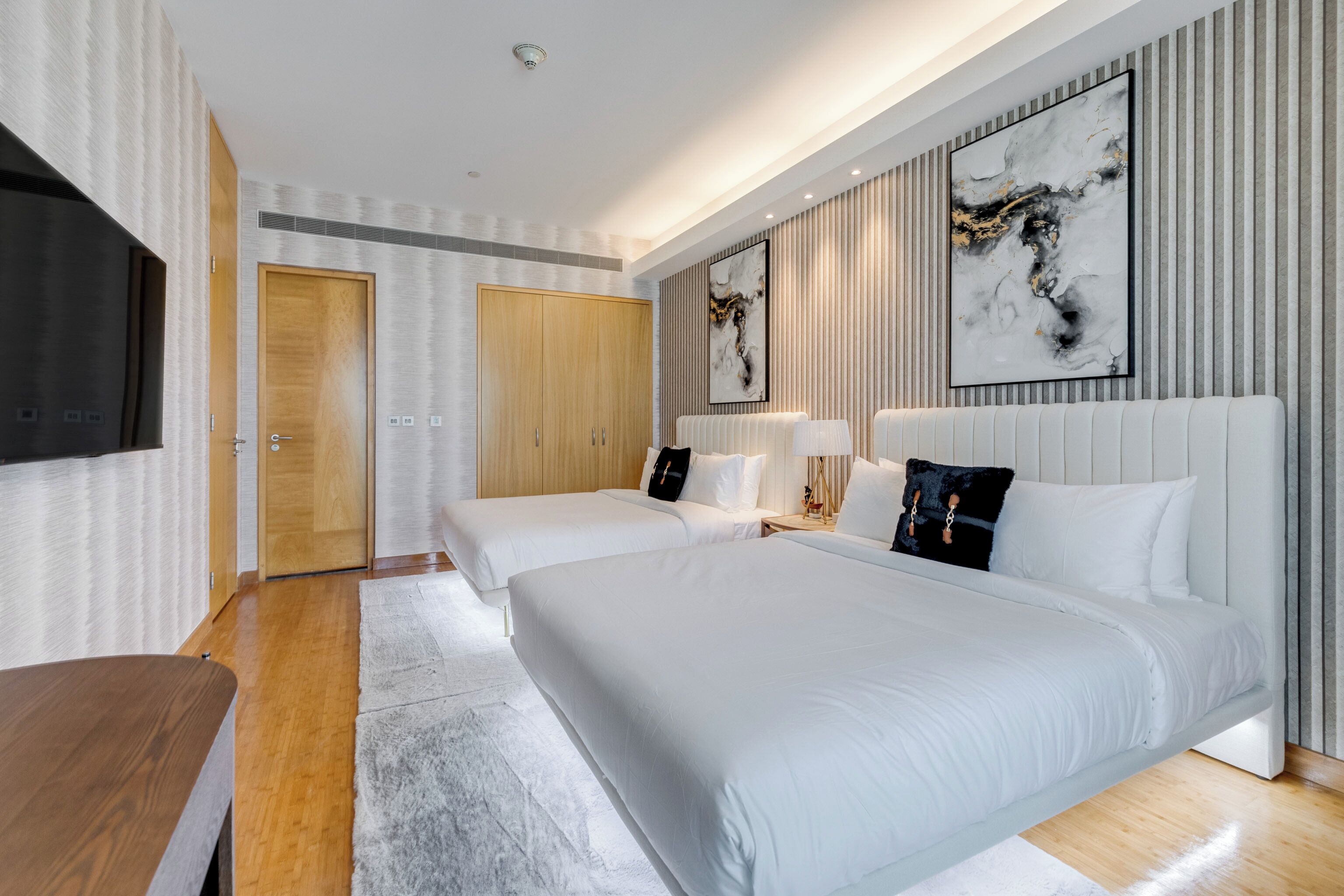 A modern hotel room with a large bed, two smaller beds, a wooden desk, and a TV.