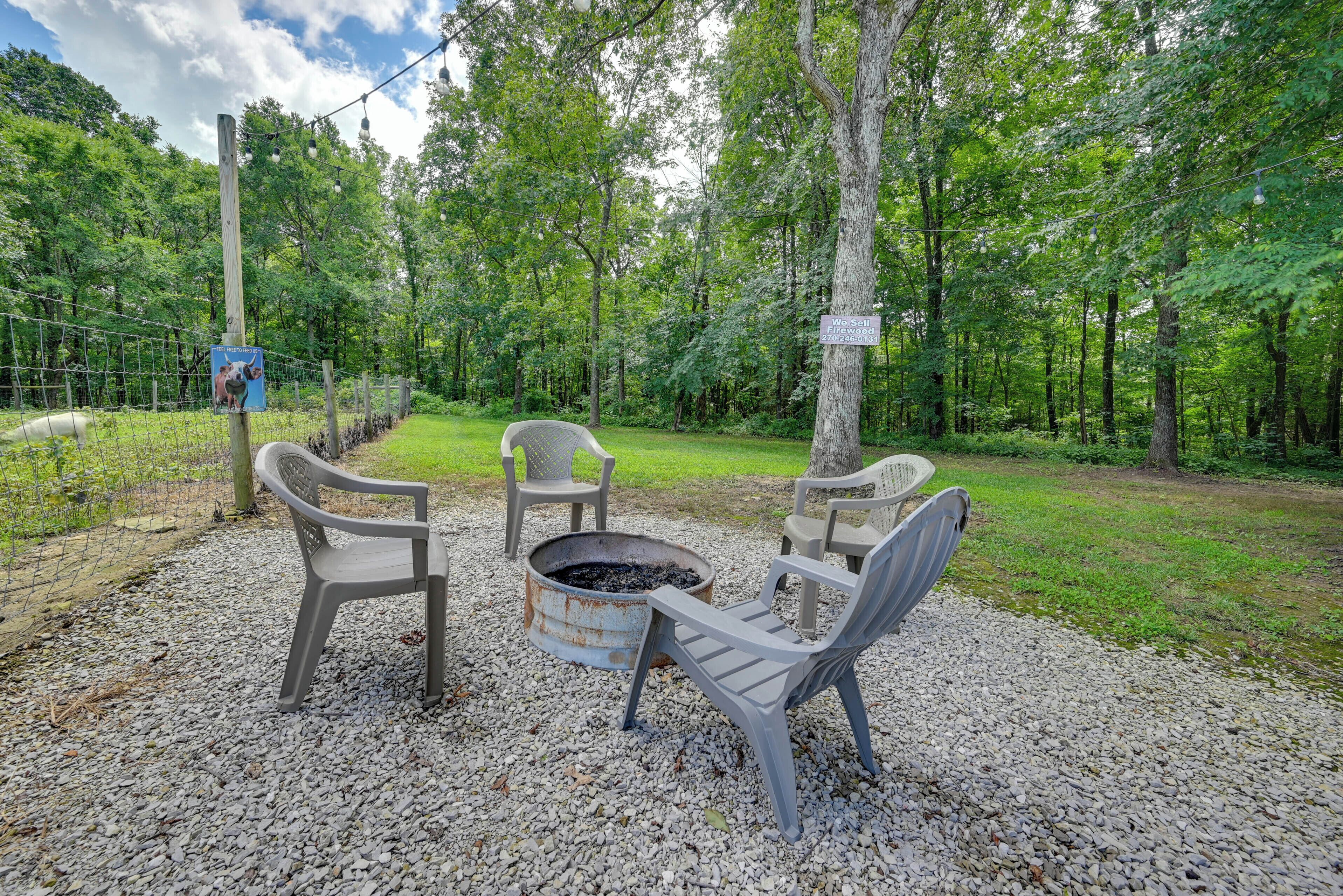 A campsite with a fire pit, two chairs, and a signpost in a wooded area.