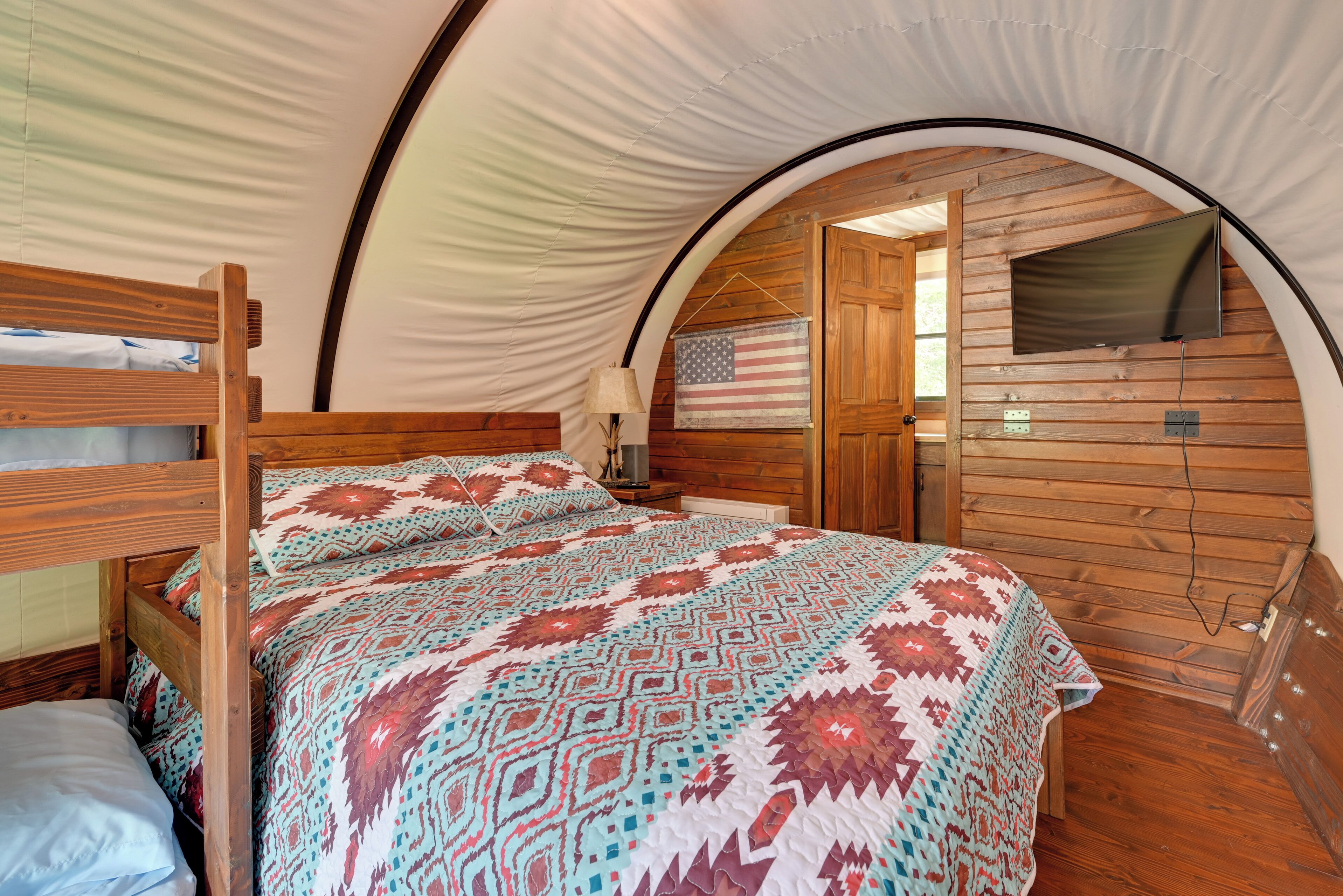 A tent-style room with a bed, an American flag decoration, a television, and wooden walls.