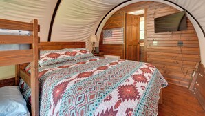A tent-style room with a bed, an American flag decoration, a television, and wooden walls. - 50-acre 'pioneers Paradise' 8 Mi to Mammoth Cave! (Brownsville)