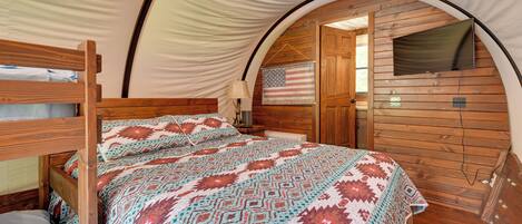 Une pièce aménagée comme une tente, avec un lit, un drapeau américain en guise de décoration, un téléviseur et des murs en bois.