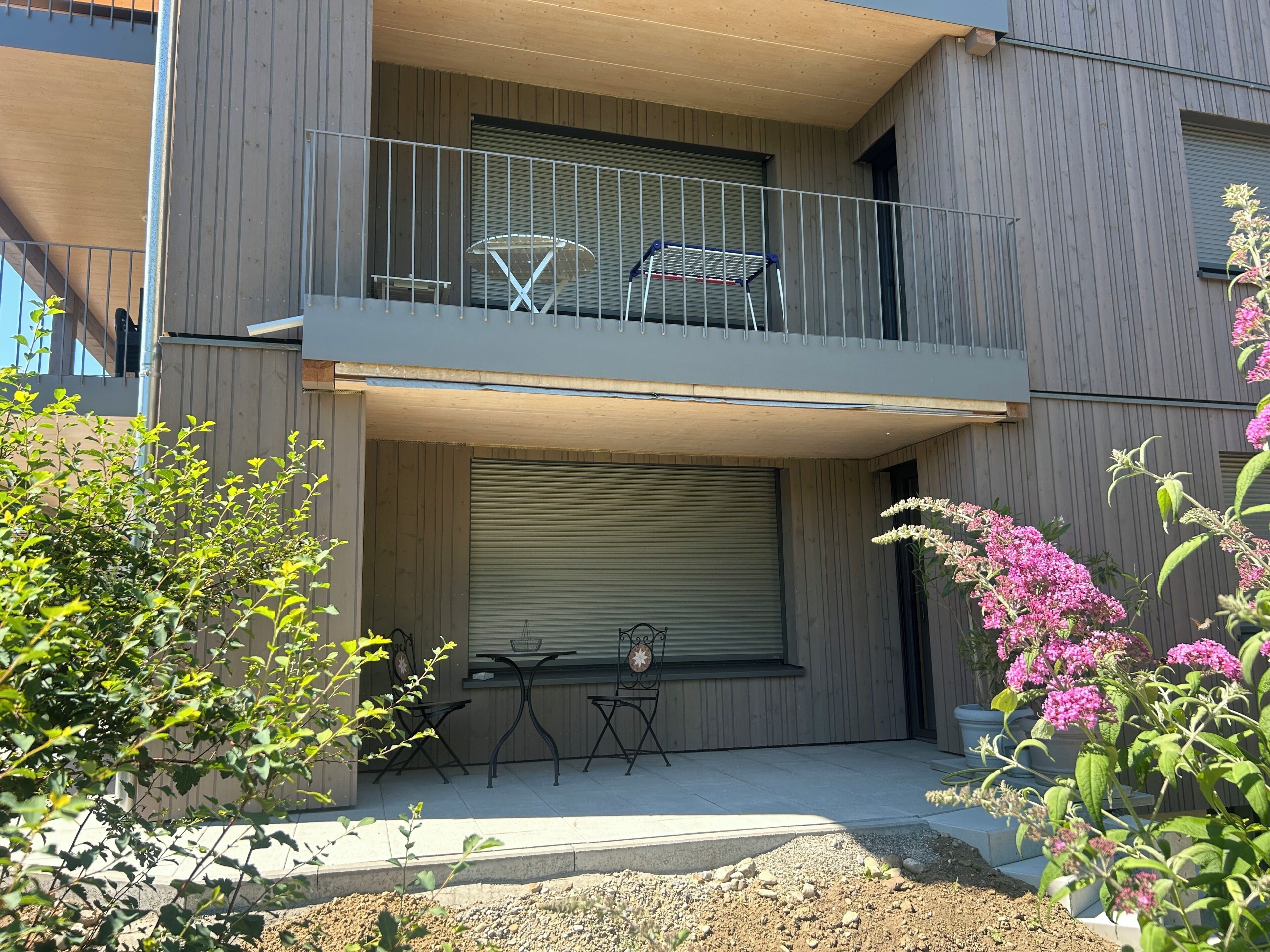 A two-story building with a balcony, outdoor seating, and potted plants.