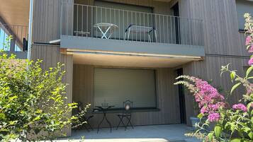 A two-story building with a balcony, outdoor seating, and potted plants.