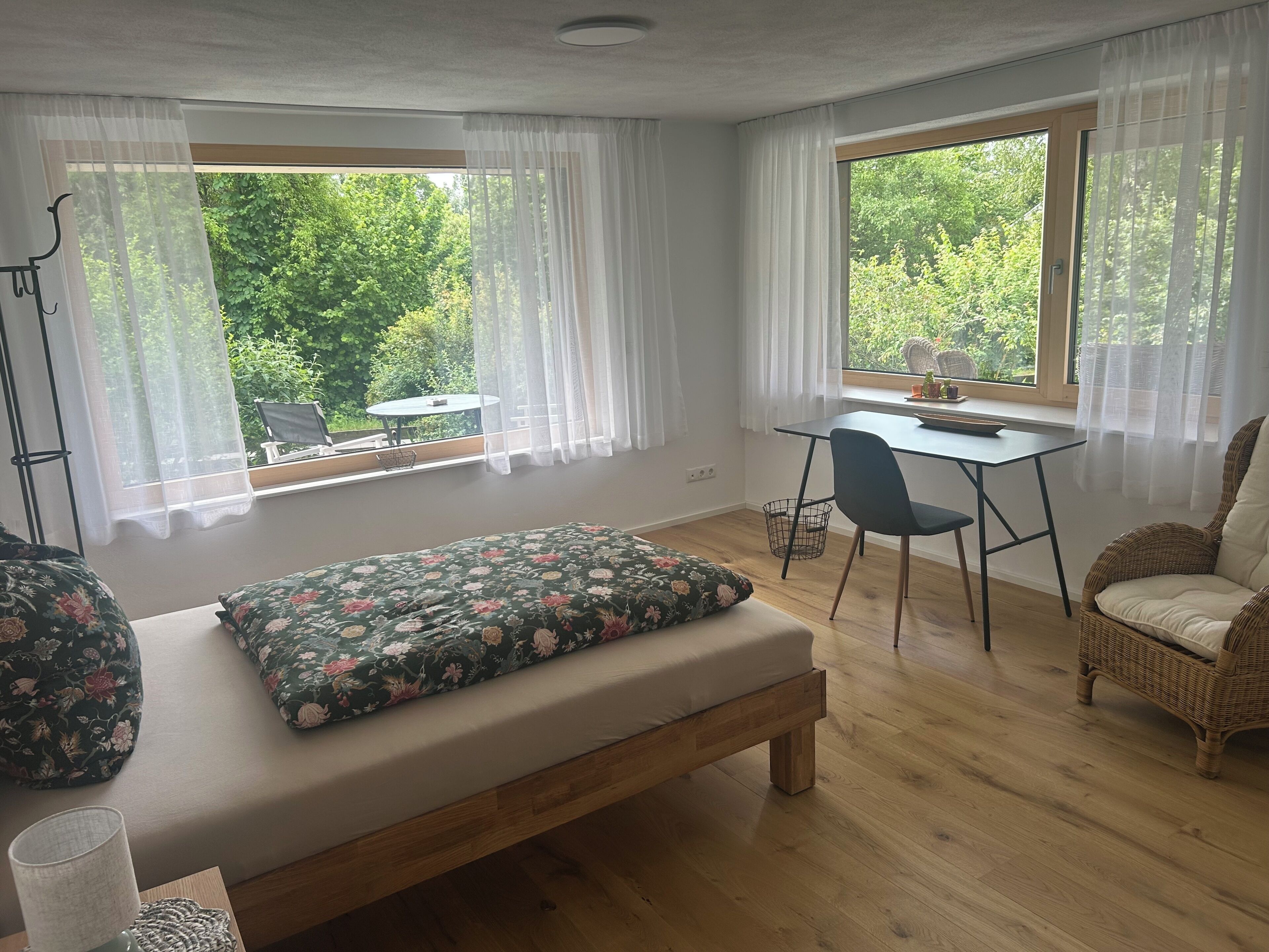 A bedroom with a bed, a desk, a chair, and a wicker chair.
