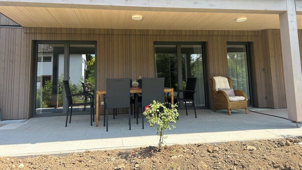 Un área de estar al aire libre techada con mesas y sillas, una planta pequeña y una silla de mimbre.
