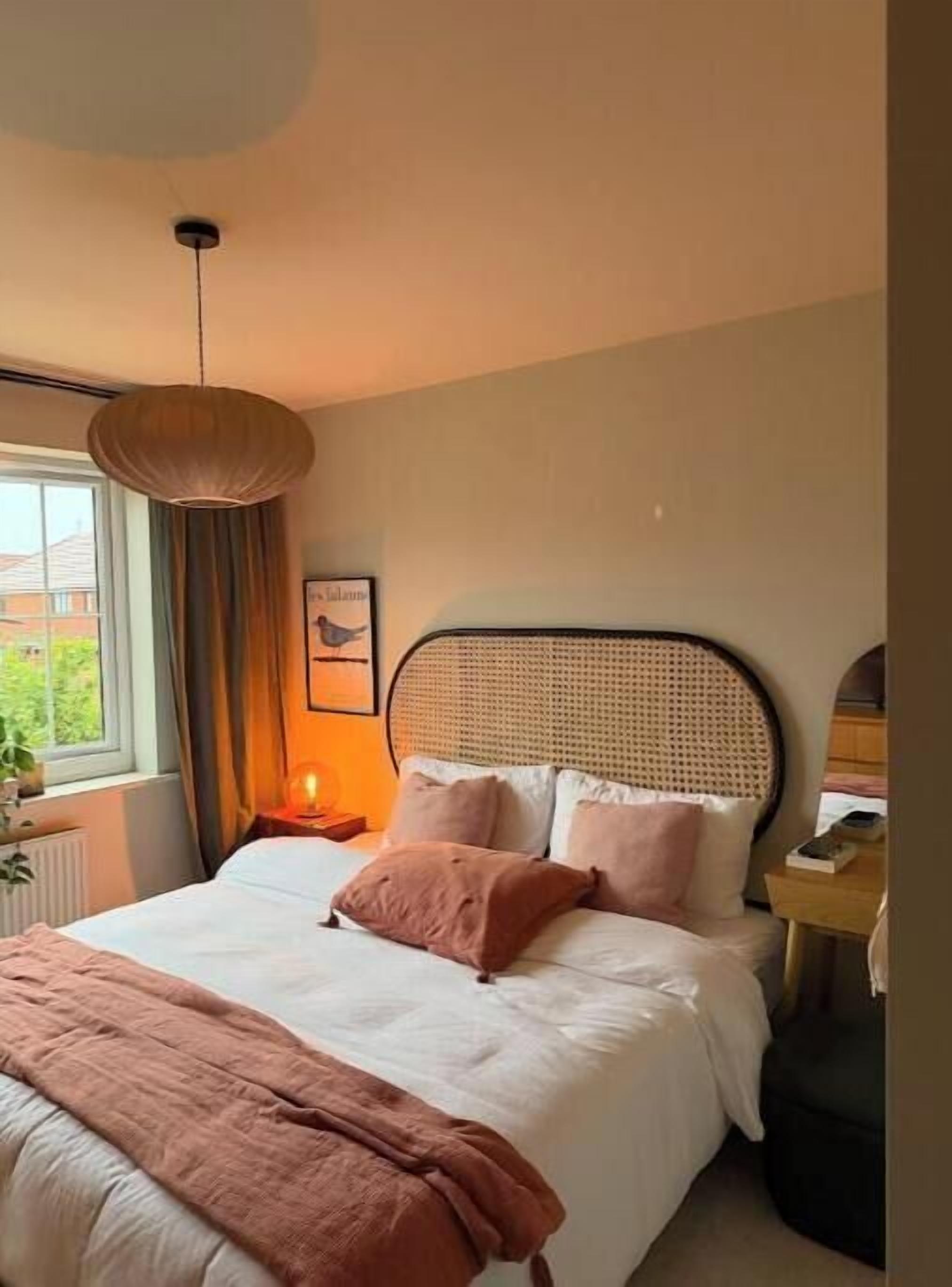 Ein Schlafzimmer mit Bett, Nachttisch, Lampe und einem Fenster mit Vorhängen.