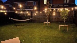 A backyard with a hammock, a small tree, and string lights. - Stylish 3-Bed Retreat Near the Peak District | Modern Comfort & Boutique Style (Burton-on-Trent)