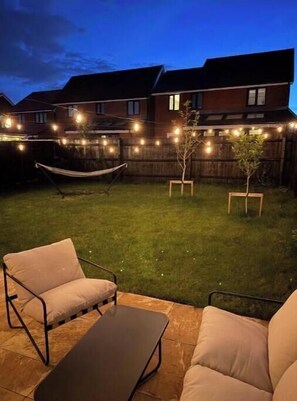 Ein Garten mit einer Hängematte, einem kleinen Baum und Lichterketten.