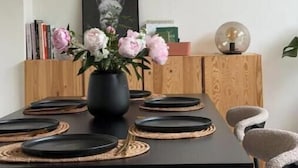 A dining area with a black table, woven placemats, and a woven ceiling light fixture. - Stylish 3-Bed Retreat Near the Peak District | Modern Comfort & Boutique Style (Burton-on-Trent)