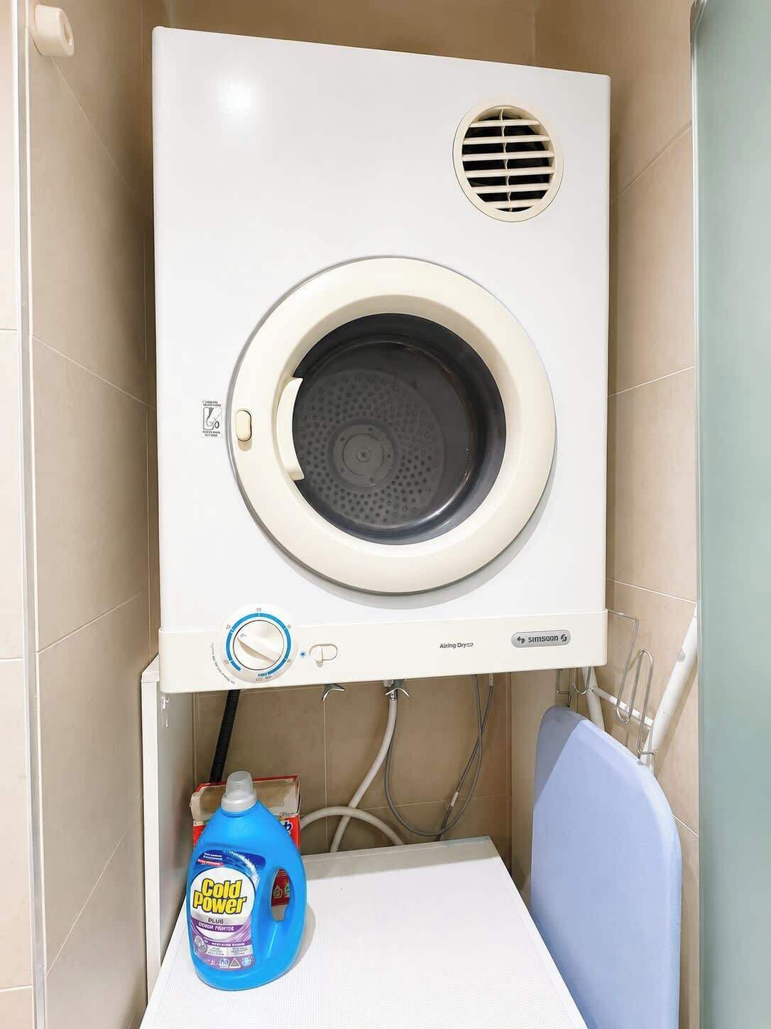 Una lavadora empotrada en la pared, con un panel de control, una botella de detergente azul y una silla azul.