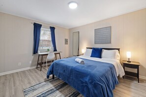 Une chambre à coucher comprenant un lit, une table de chevet, un bureau, une chaise et une fenêtre avec des rideaux.