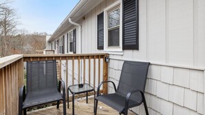 A deck with two chairs and a small table, a wooden railing, and a white building with black shutters. - Tranquil 1-bedroom apartment with AC in vibrant Durham (Durham)