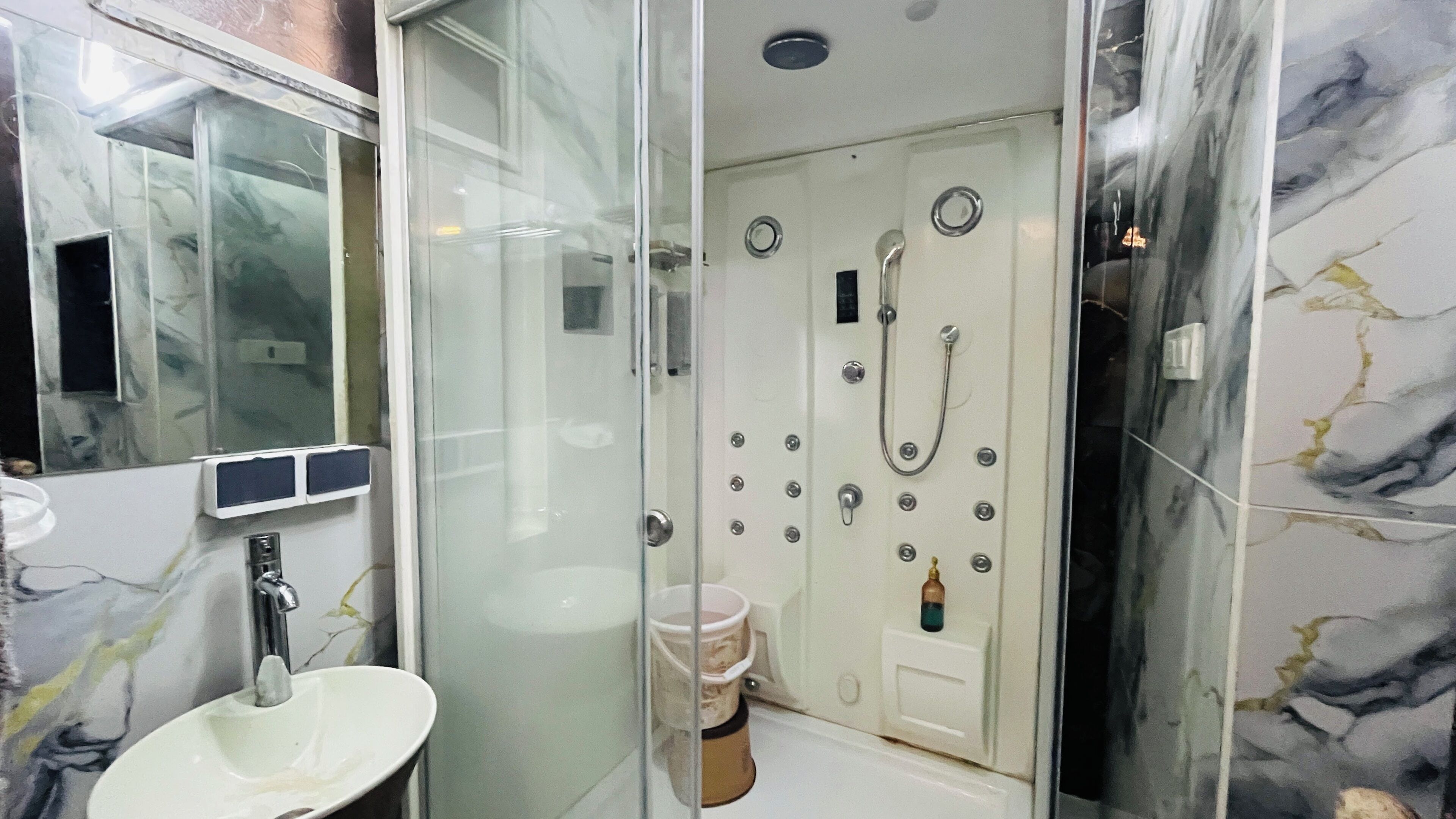 Un baño con cabina de ducha de vidrio, un lavabo blanco y una pared de mármol.