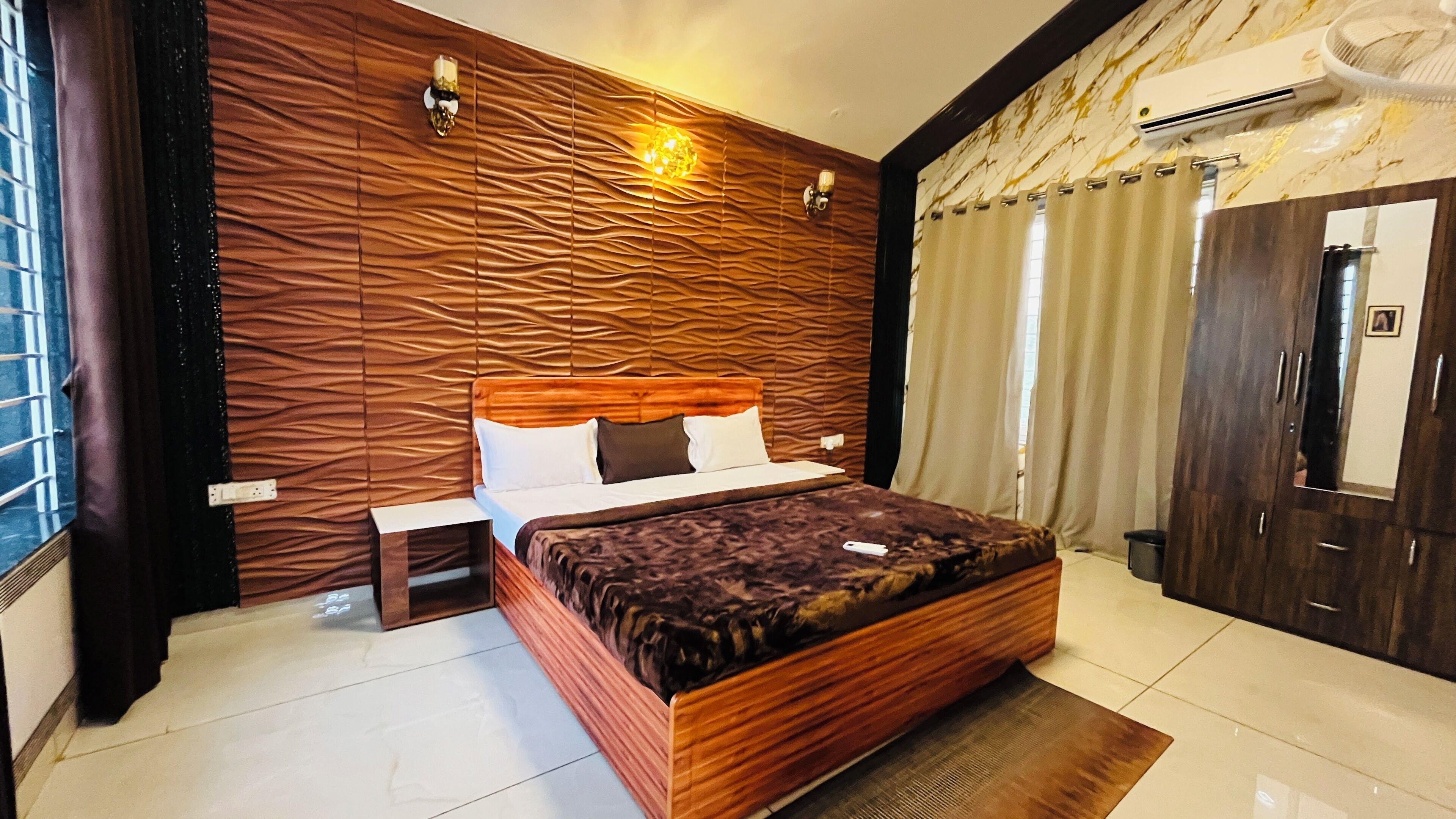 Un dormitorio con cabecera de madera, cama con colcha oscura estampada, mesita de noche y lámpara de pared.