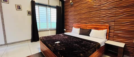A modern bedroom with a wooden headboard, a bed with white linens, a nightstand, and a view of the sea through a window.