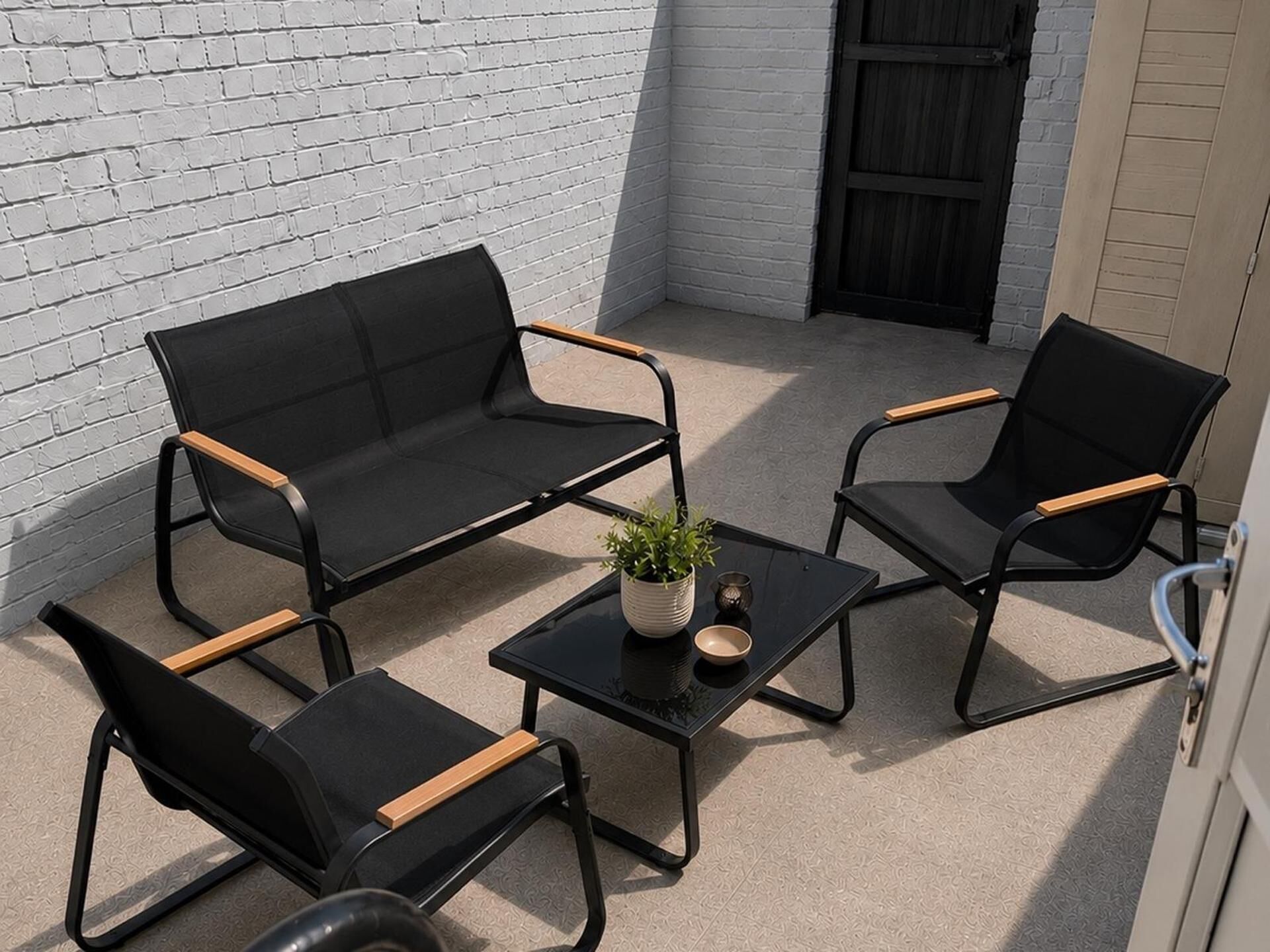 A patio with a black sofa set, two armchairs, and a small table with a plant.