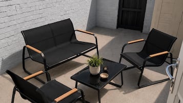 Een terras met een zwarte zithoek, twee fauteuils en een bijzettafeltje met een plant.