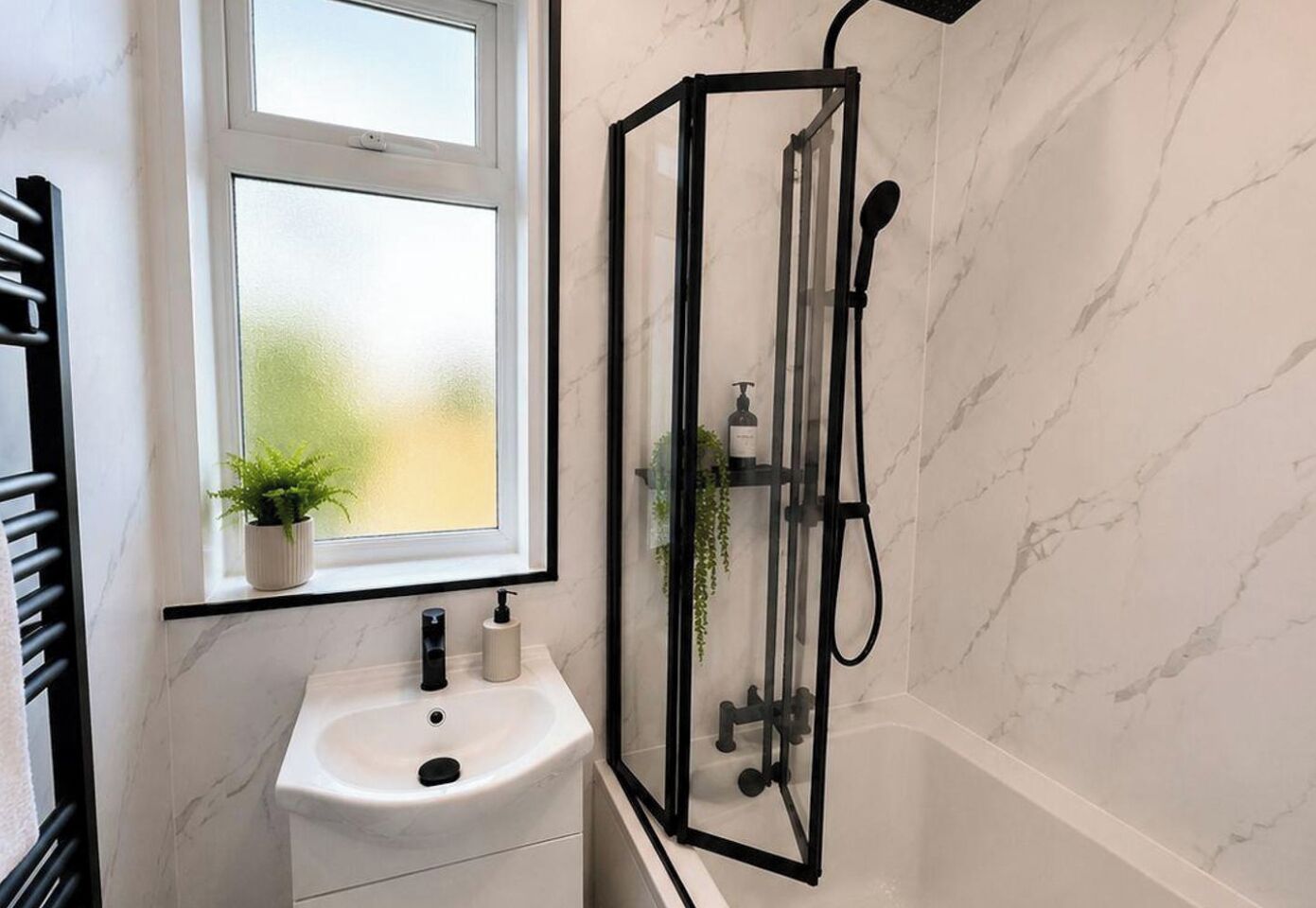 A bathroom with a white marble sink, a window with a plant, and a glass-enclosed shower.