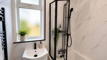 A bathroom with a white marble sink, a window with a plant, and a glass-enclosed shower.