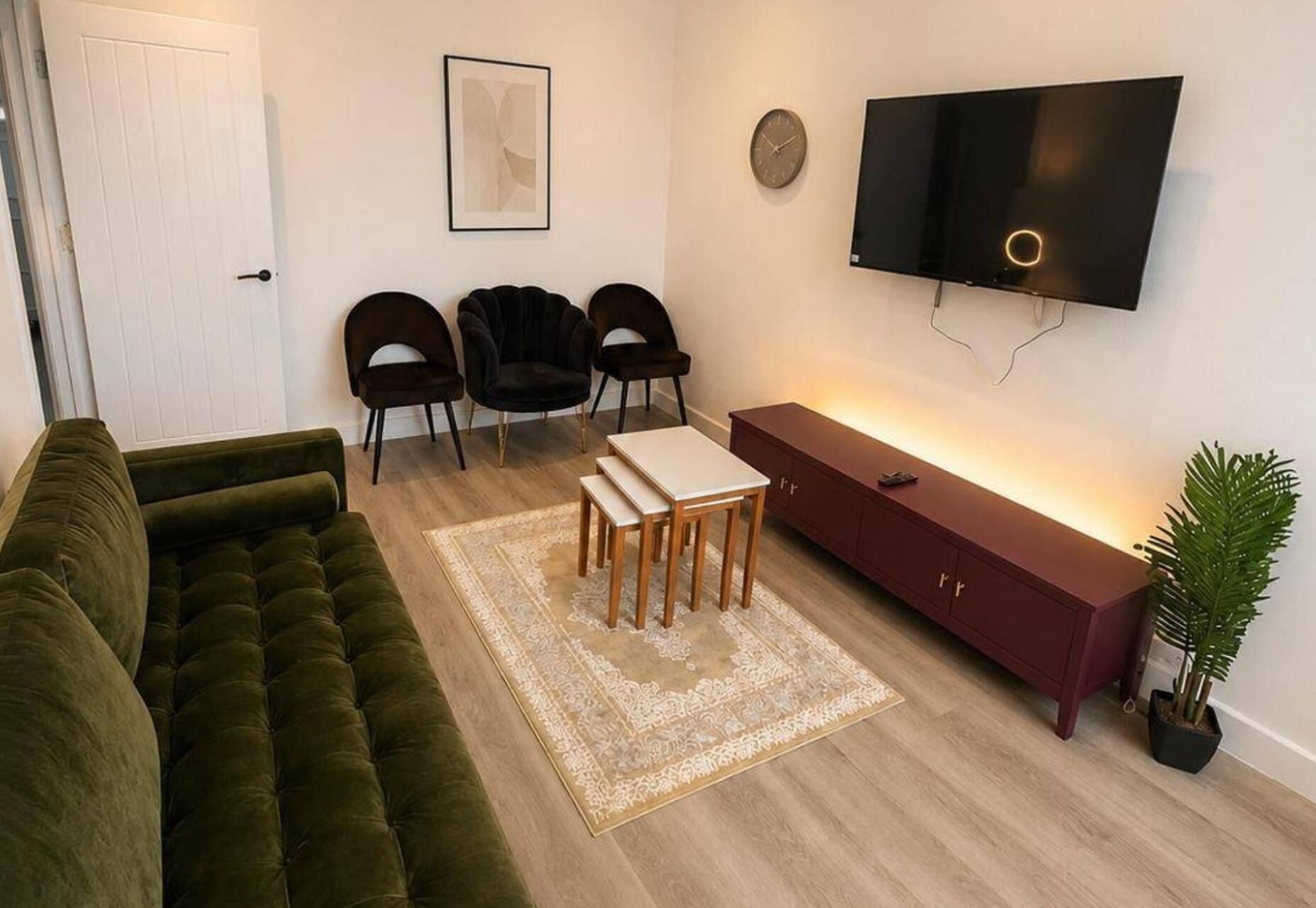 A living room with a green sofa, a wooden coffee table, a red cabinet, a TV, and a clock on the wall.