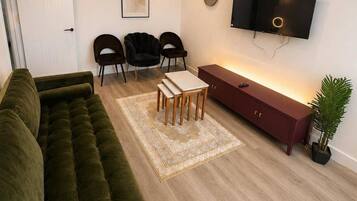 A living room with a green sofa, a wooden coffee table, a red cabinet, a TV, and a clock on the wall.