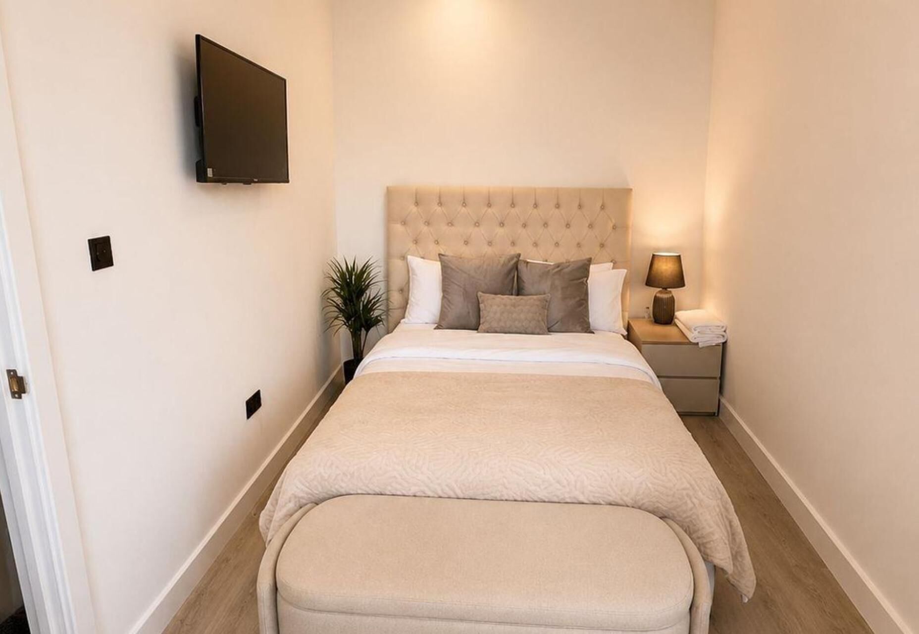 A bedroom with a bed, a nightstand, a lamp, and a TV mounted on the wall.