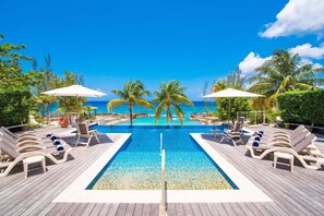 A wooden deck with a pool, lounge chairs, and umbrellas. - Casa Luna 4: Gated Luxury Near 7Mile Beach w/Pool, Heated Spa, and Private Beach Cove (Grand Cayman)